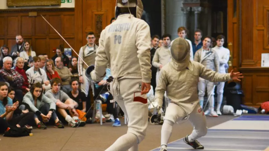 Two fencers competing with a large crowd watching on