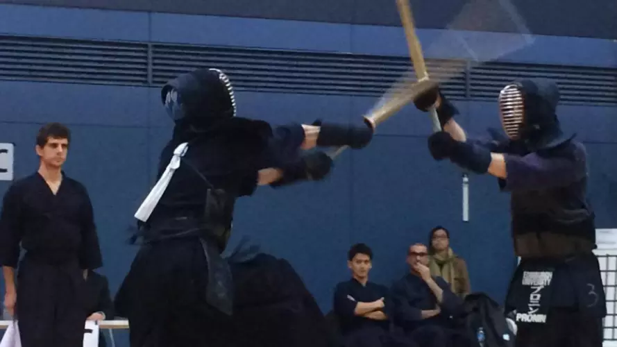 Two people in a kendo duel with a crowd watching behind them