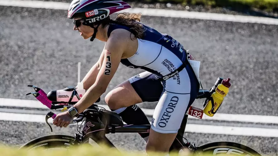 A triathlete riding her bike along a road, wearing Oxford dark blue kit
