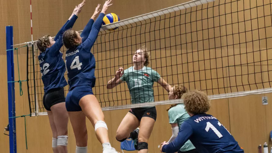 Two female volleyball players jumping to block in the Oxford vs Cambridge Varsity match